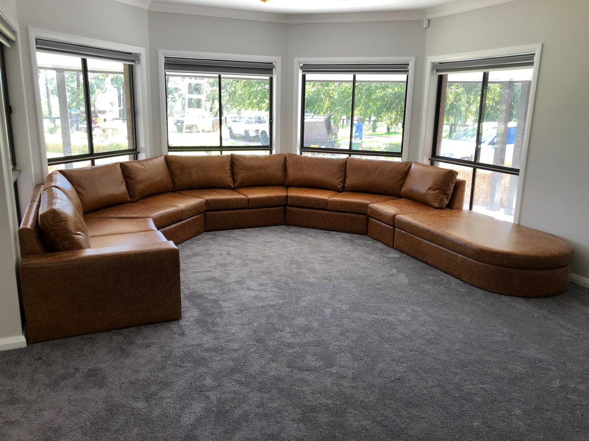 Caramel-coloured custom bay window lounge following the room’s curved window layout, with a rounded chaise end.