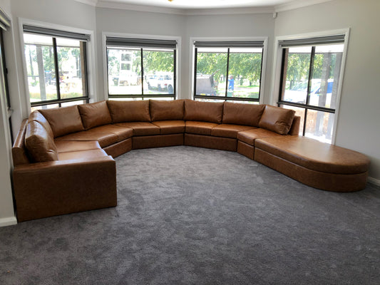Caramel-coloured custom bay window lounge following the room’s curved window layout, with a rounded chaise end.