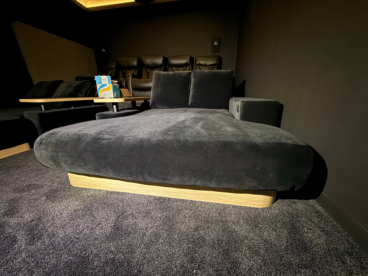Real custom DreamCloud daybed with two taller reclining-back cushions, charcoal upholstery, timber plinth and floating table in a home cinema.